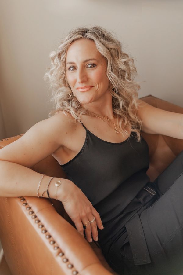 Confident woman with curly blonde hair sitting in a leather armchair.