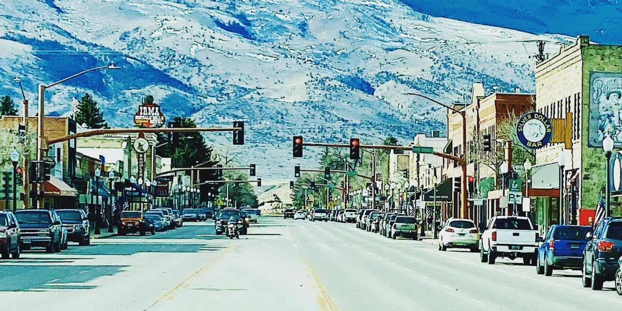 A street in Cody, WY with businesses on each side and mountains in the background.