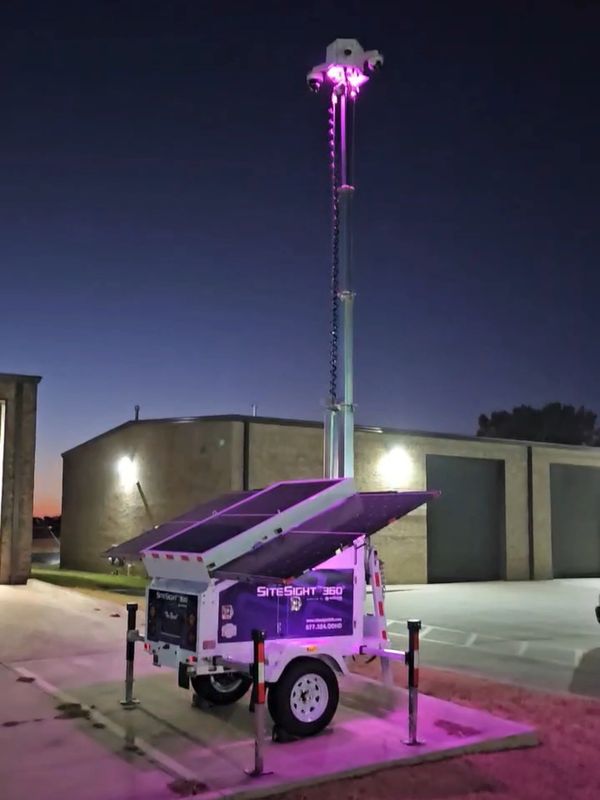 Portable SiteSight 360 security camera tower illuminated with purple lights at dusk.