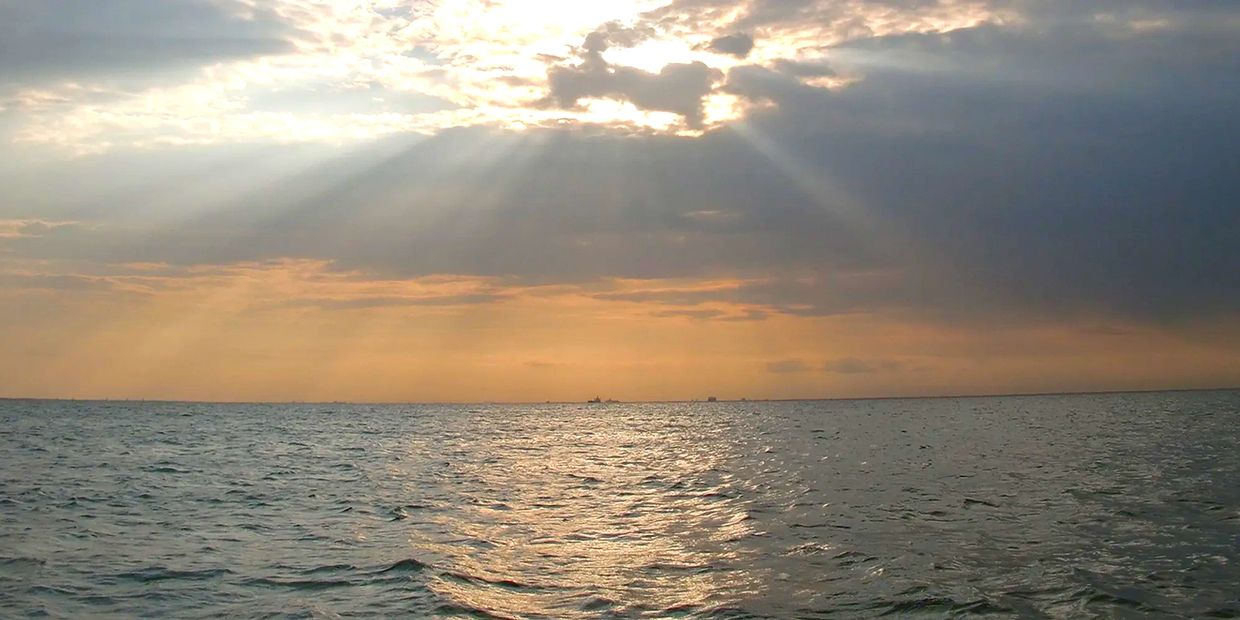 Sun rays breaking through clouds over a calm sea.