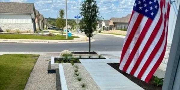 A modern front yard with gravel, plants, and an American flag.