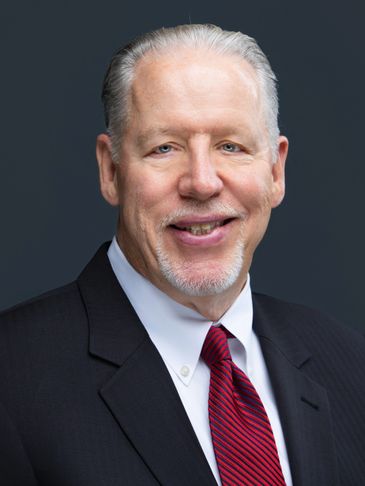 Professional portrait of an older man in a suit and red striped tie.