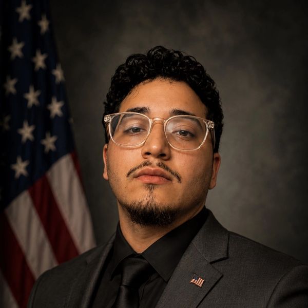 Professional portrait of a man in a suit with an American flag.
