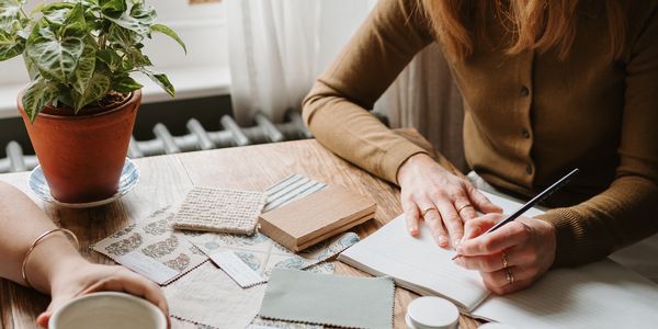 Person writing in a notebook surrounded by crafting materials.