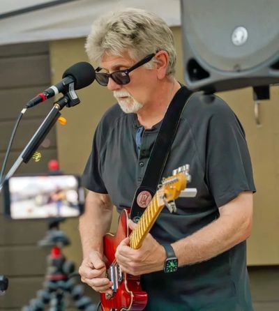 Older man playing electric guitar and singing into microphone.