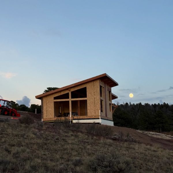 Wooden house under construction on a hill with a full moon in the background.