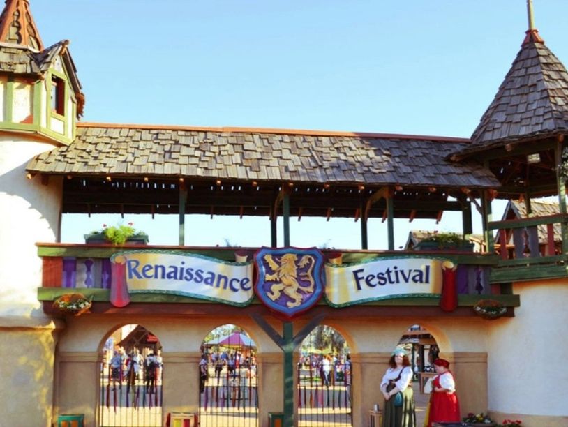 Entrance to a lively Renaissance Festival with people in period costumes.