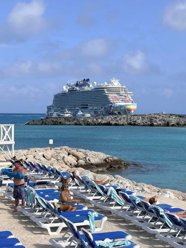 Cruise ship near a beach with sunbathers on lounge chairs.