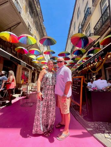 Couple posing under colorful umbrellas on a vibrant street.