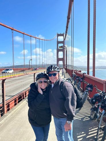 A couple wearing helmets posing on the Golden Gate Bridge with bikes nearby.