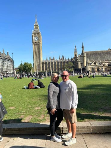 A couple posing near Big Ben and the Houses of Parliament in London on a sunny day.