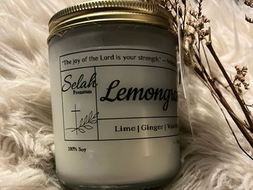 A lemongrass scented soy candle with a gold lid on a fluffy white surface.