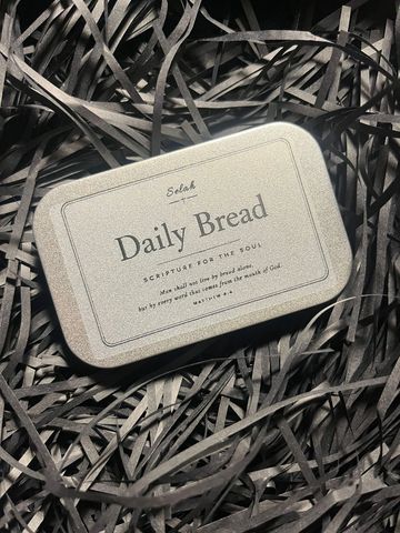 A tin box labeled Daily Bread on shredded black paper.