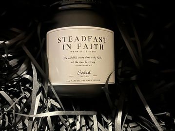 Candle labeled 'Steadfast in Faith' with warm spice scent in shredded paper.
