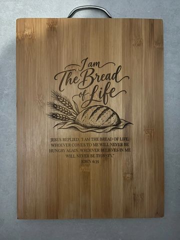 Wooden cutting board with a religious quote and bread illustration.