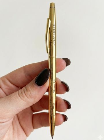 Hand holding a gold-colored pen with inscription.