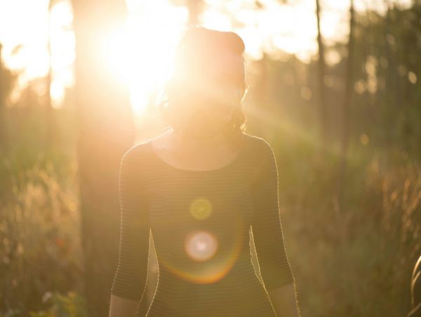 Person silhouetted against bright sunlight in a forest.