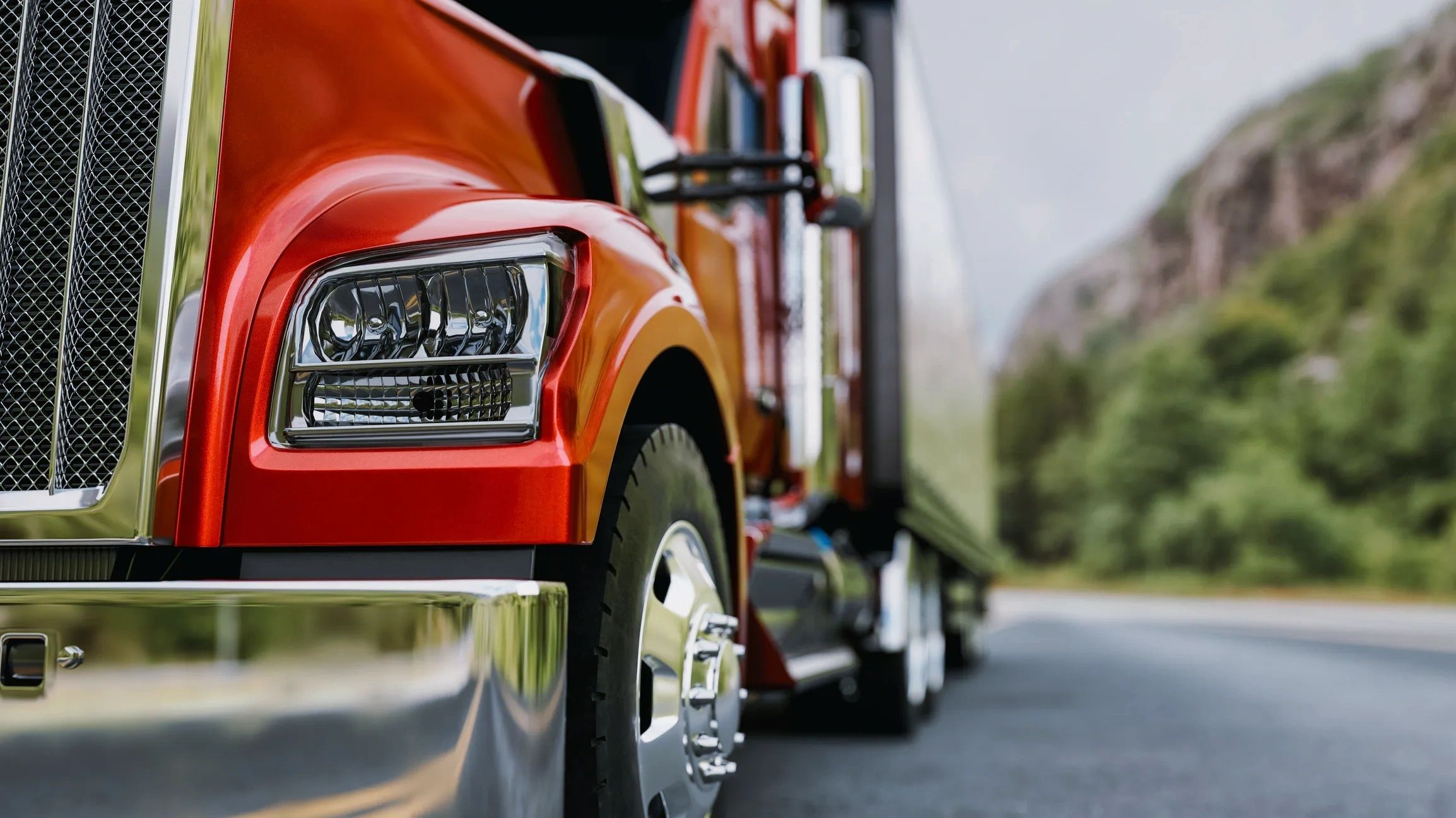 Close-up of a shiny red semi-truck on a road with a blurred natural background.