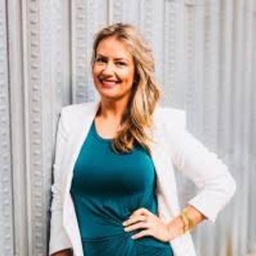 Smiling woman in white blazer and teal dress.