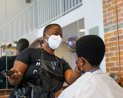 Hairstylist cutting clients hair with mask on.