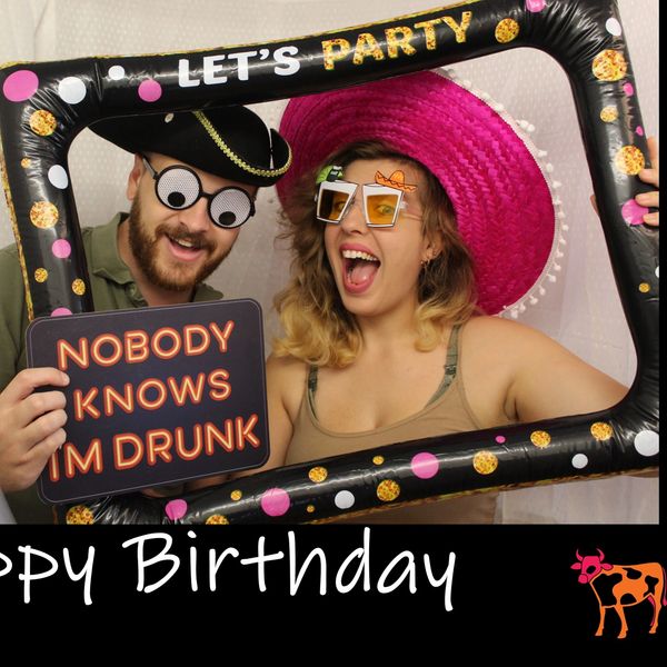 Two people celebrate with funny props and a birthday frame.