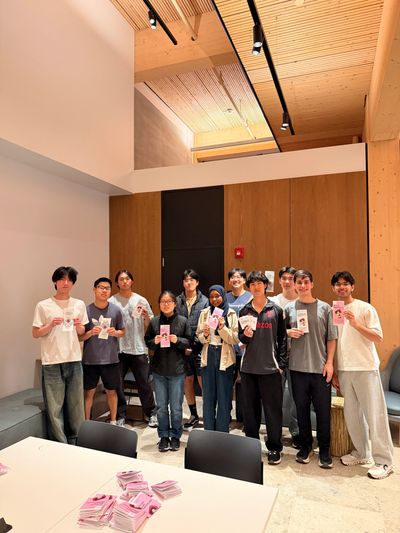 A group of young people posing indoors with pink flyers in hand.