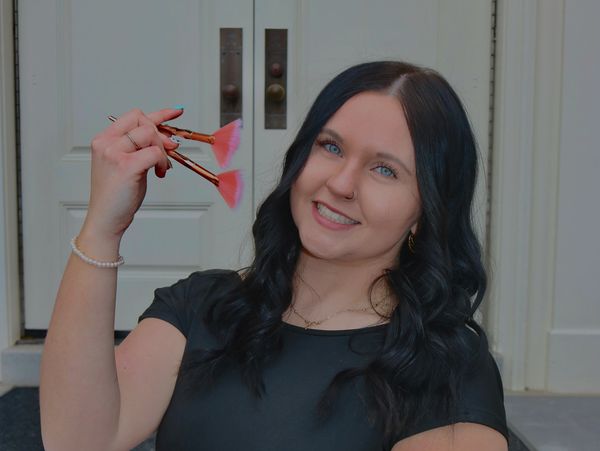 Woman smiling and holding pink makeup brushes.