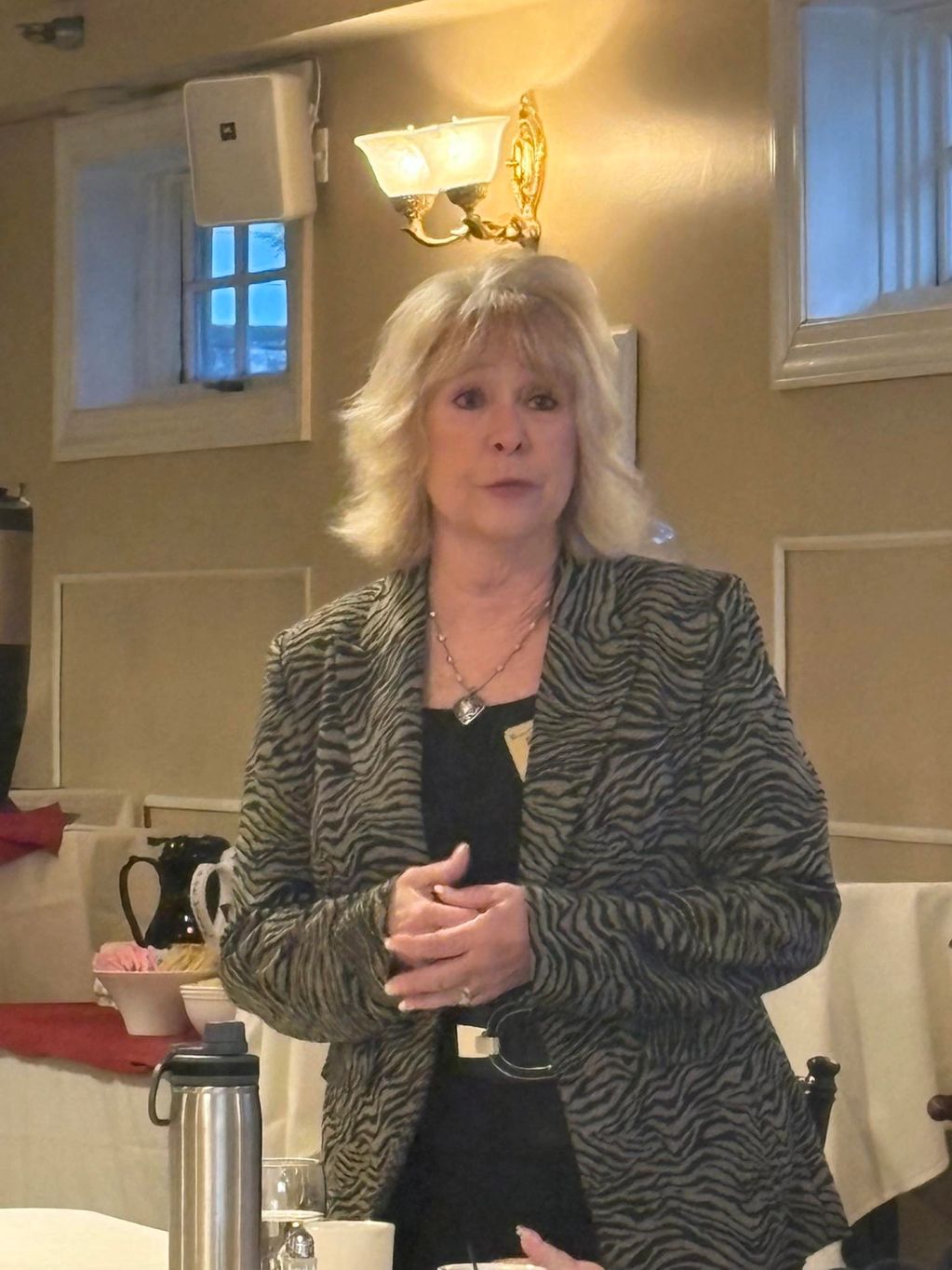 Woman in zebra print jacket speaking indoors.