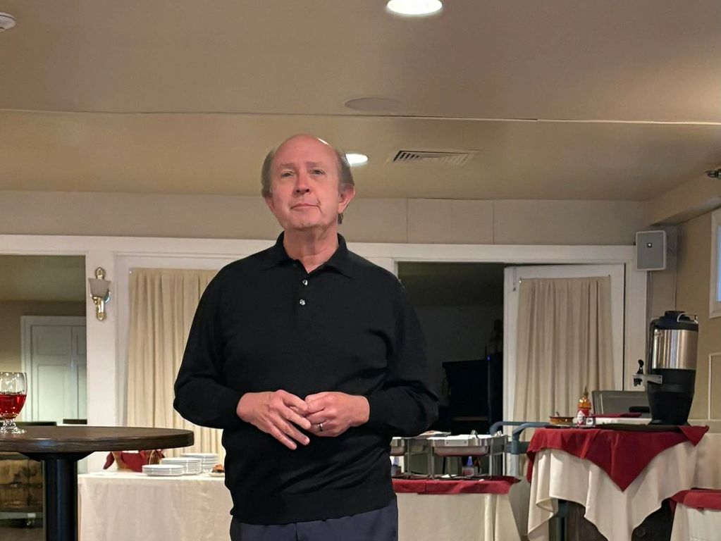 Man in black sweater standing in a room with tables and refreshments.