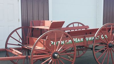 Antique red wooden wagon with large spoked wheels labeled Putnam Hardware Co.