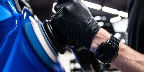 Person polishing a blue car with a buffer wearing black gloves.