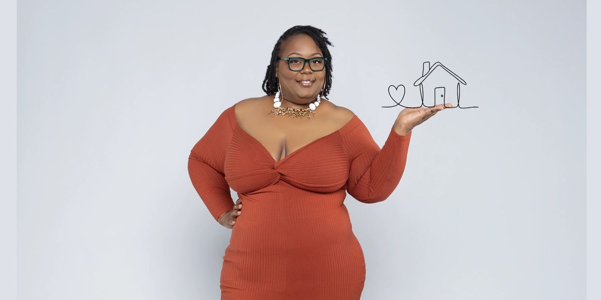 Confident woman in rust dress holding drawn house and heart.