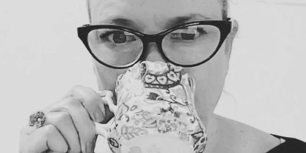 Woman wearing glasses drinking from a decorative teacup.