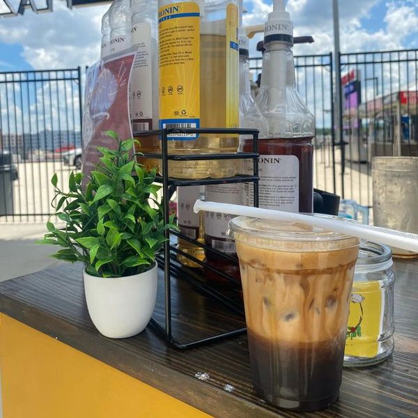 Iced coffee with syrup bottles and a small plant outdoors.