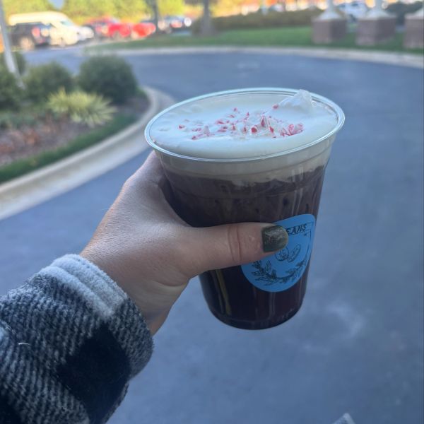 Hand holding iced coffee with whipped cream and peppermint.