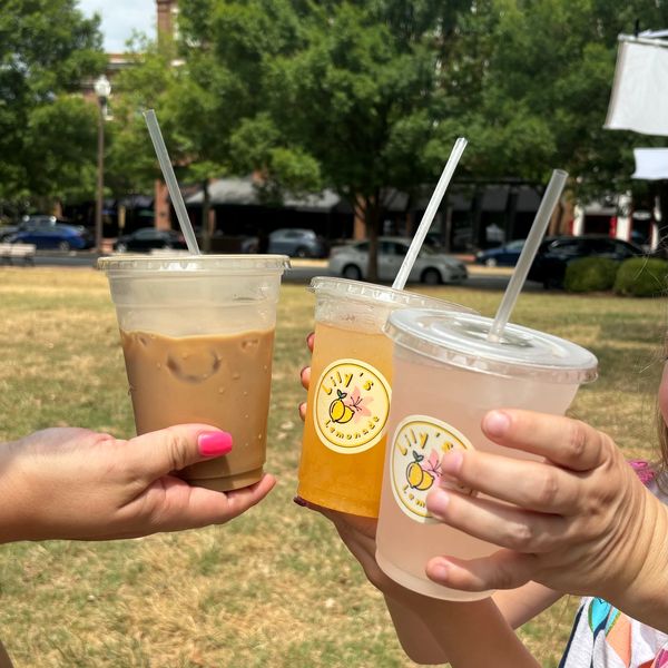 Three cold drinks held outdoors in clear plastic cups.