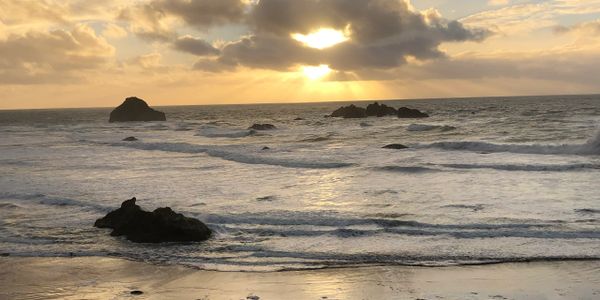 Sunset over rocky ocean waves with dramatic clouds.