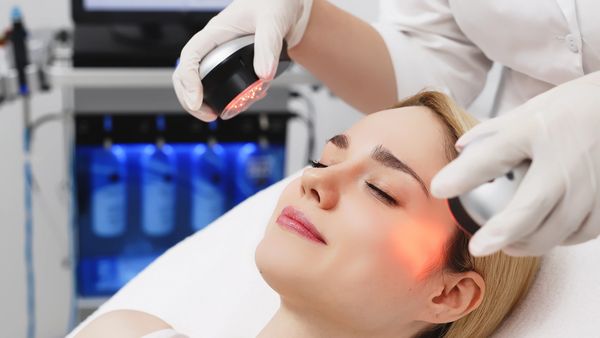 A woman receiving facial red light therapy from a technician wearing gloves