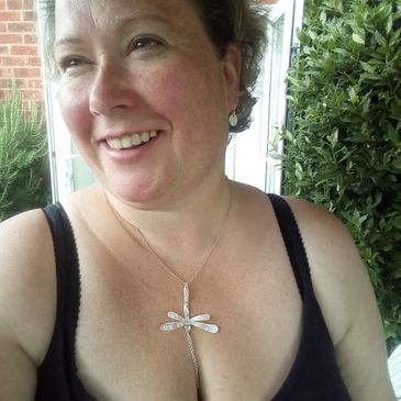 Picture of Angela Humphrey smiling, wearing a dragonfly pendant and medium stud earrings.