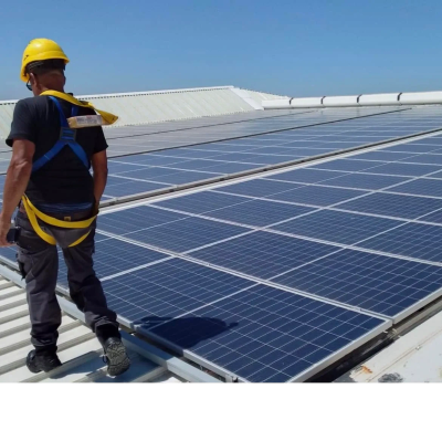 A worker installing solar panels on a roof, wearing safety gear.