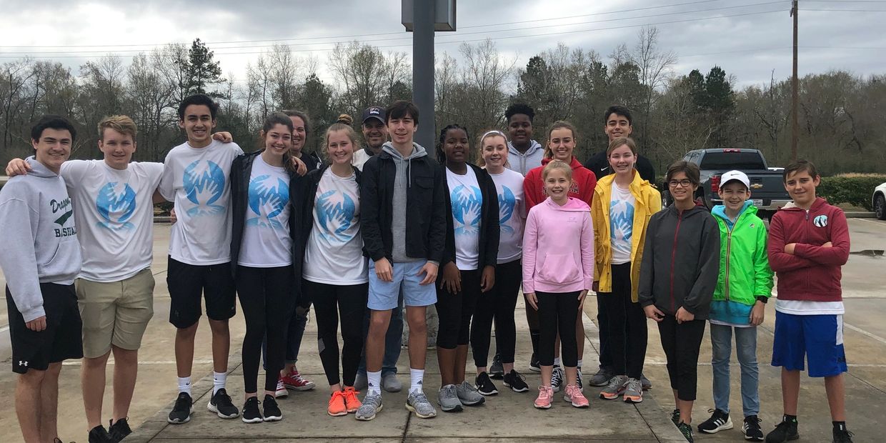 Group of teenagers and adults posing outdoors in casual and sportswear.