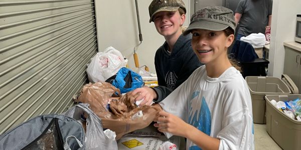 Two boys smiling while packing bags indoors.