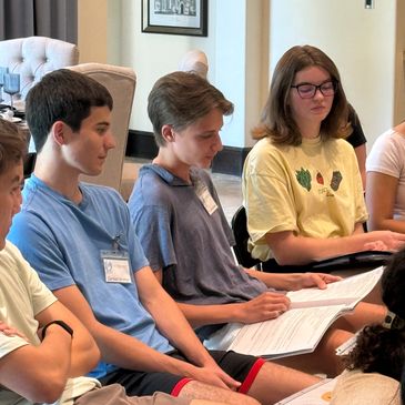 Teenagers sitting and reading papers in a group setting.