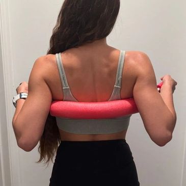Woman exercising with a pink resistance band, showing her back muscles.