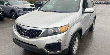 Silver Kia SUV with front bumper damage parked in a lot.