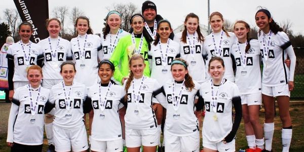 Youth soccer team in white uniforms posing with medals outdoors.