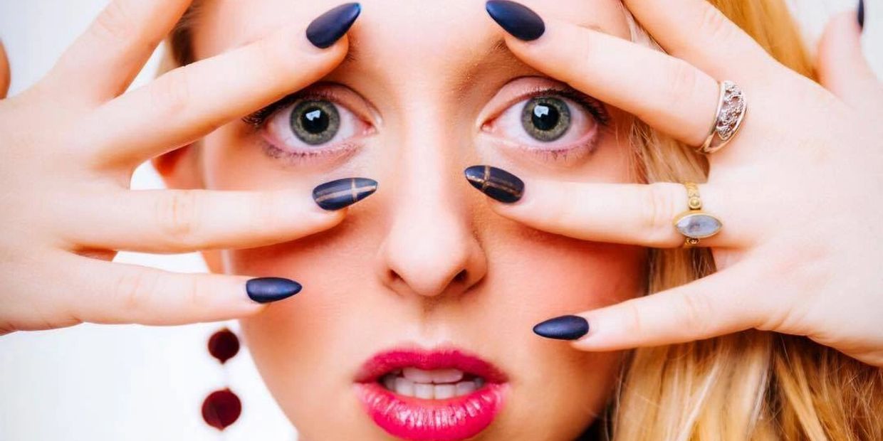 Close-up of a woman with black nail polish framing her eyes.
