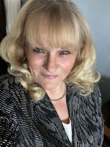 Smiling woman with blonde curly hair in a patterned black jacket.