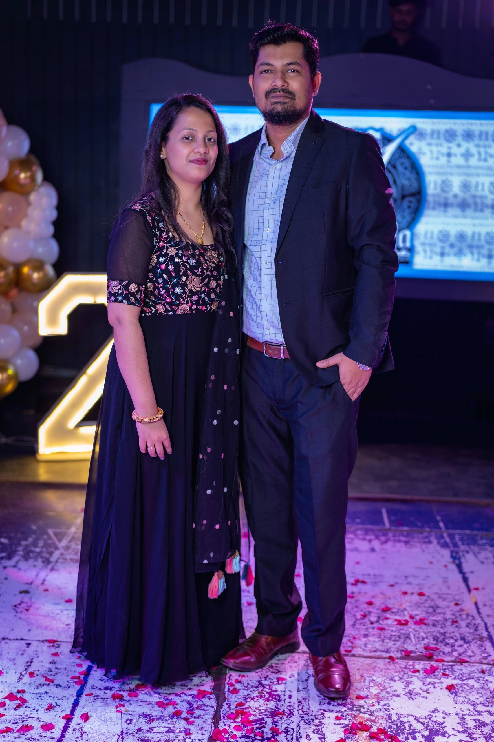 Couple dressed elegantly, posing at a festive event with rose petals on the floor.