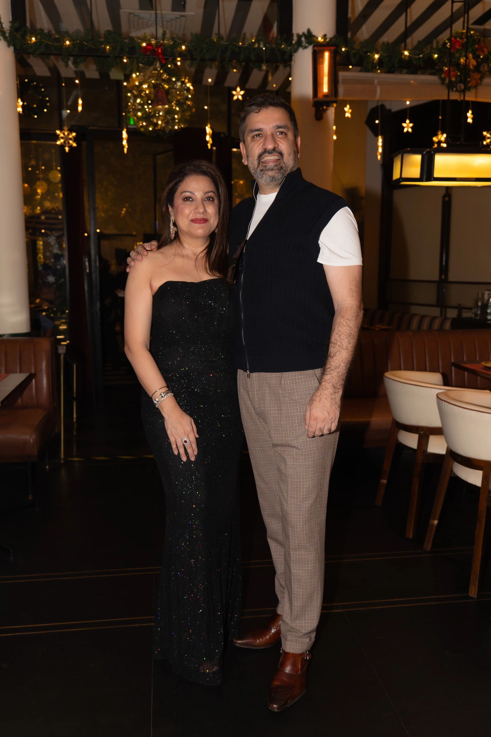 Couple dressed elegantly with festive holiday decorations in the background.